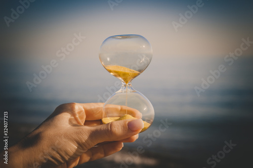 Sand in the hourglass and sand on the sea, time in the hands of a young girl, the concept of falling grains of sand in a glass flask