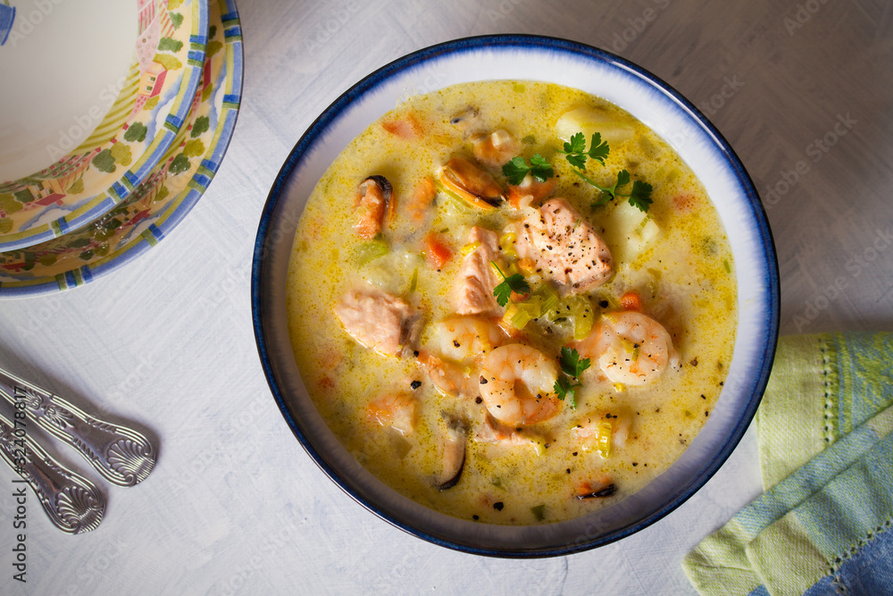 Bowl of seafood chowder with salmon on white background. Flat lay image