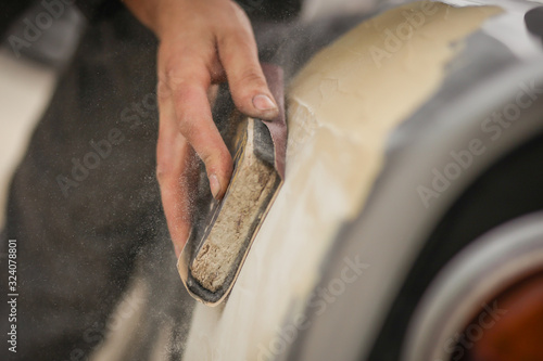 Obraz na plátně A hand of a man is seen sanding an old vintage car using a block of wood and brown sand grit paper