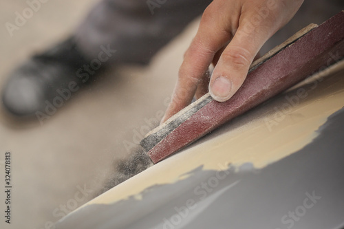 Photography A hand of a man is seen sanding an old vintage car using a block of wood and brown sand grit paper