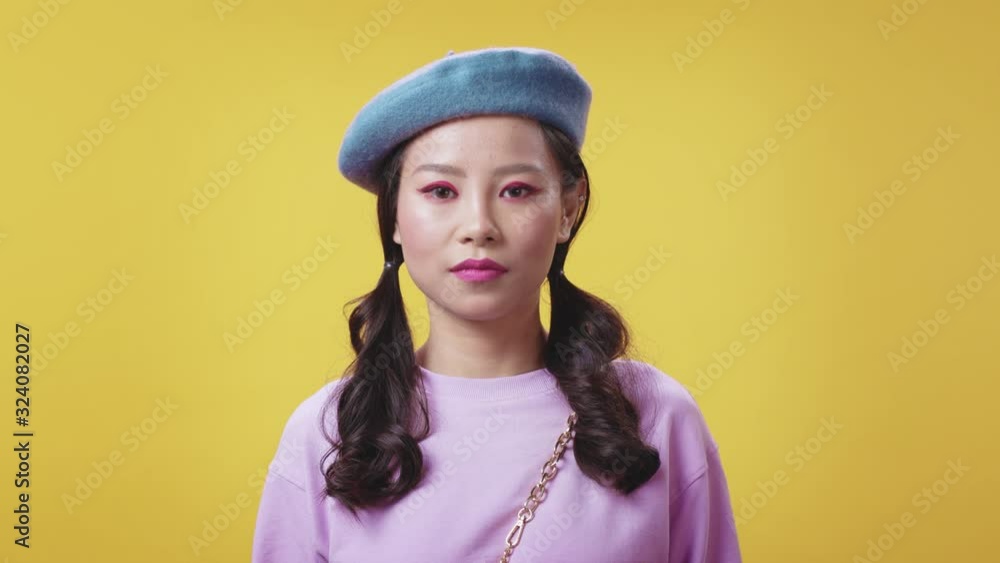 Appealing cute young korean girl in fashion looking serious at camera wearing hat stylish clothes posing on yellow background. Appealing cute young korean girl in fashion looking serious at camera wearing hat stylish clothes posing on yellow background.