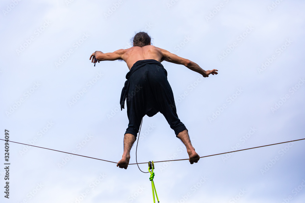 A close up and low angle view of a high wire performer balancing on a slackline, barefooted tightrope walker, topless gymnast man with copy space to sides