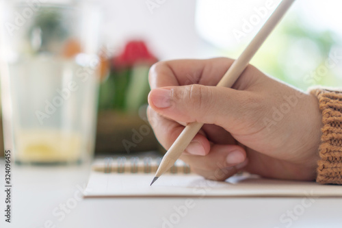 Woman hand write down in white memo notebook for take a note not to forget, to do list or plan for work in future on work table.