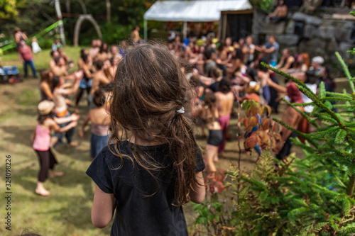 A little girl is seen from the back, as a blurry group of adults practice sacred mindful dance in background at a festival celebrating diverse culture