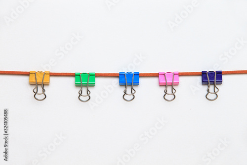 Office clips tied to a strap. Colored clothes pins on a chamois string. clorful clips on leather string isolated on white background.