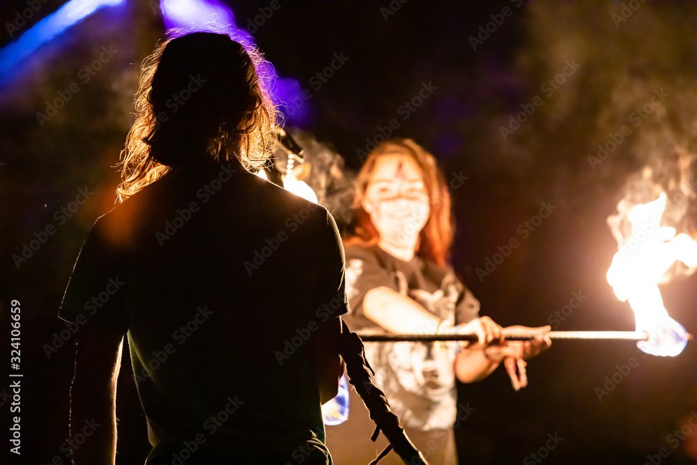 Fototapeta premium A selective focus shot of fire performers using a burning lance by night at a festival celebrating artisans, earth and alternative communities