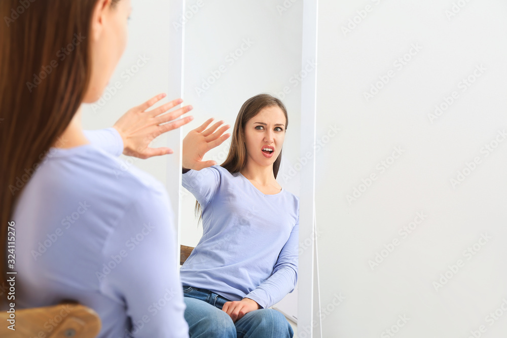 Displeased young woman looking in mirror at home Displeased young woman looking in mirror at home