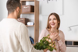 Beautiful young woman receiving flowers from her boyfriend on romantic date at home