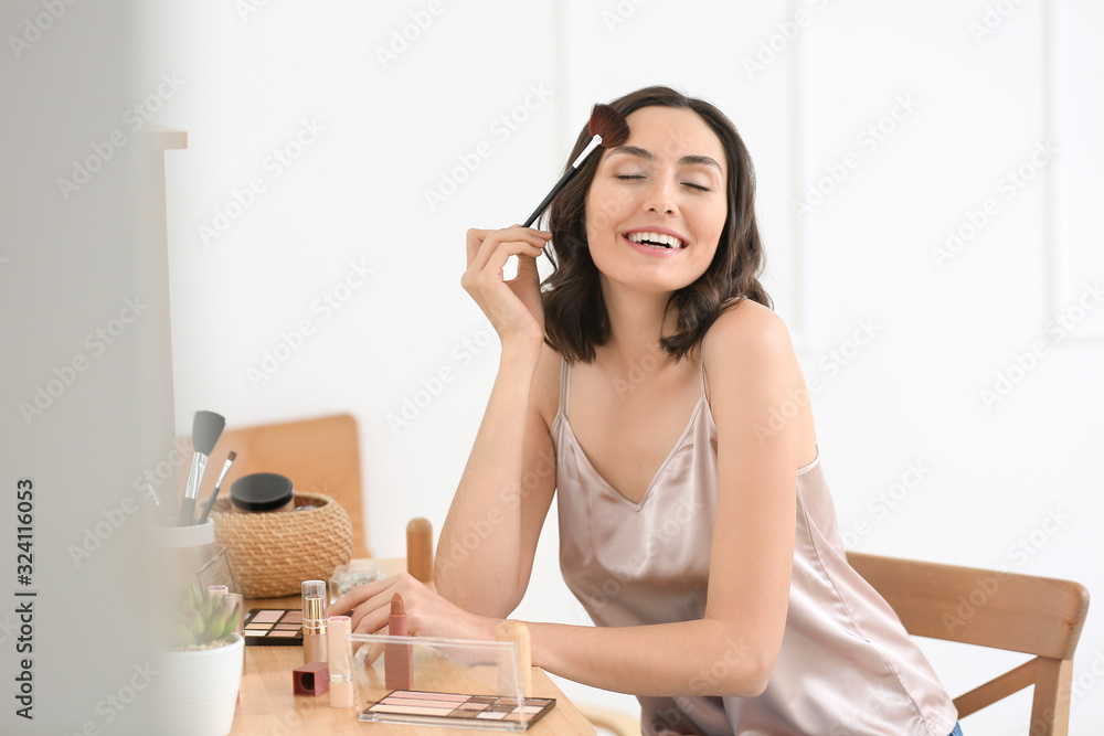 Beautiful young woman applying makeup at home