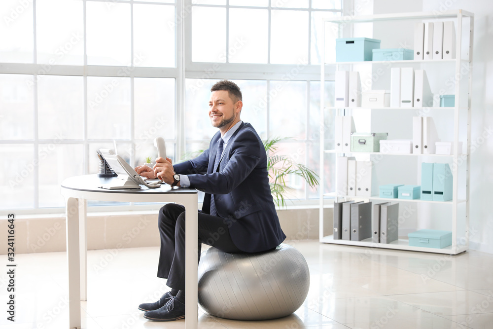 Businessman sitting on fitness ball while working in office Businessman sitting on fitness ball while working in office