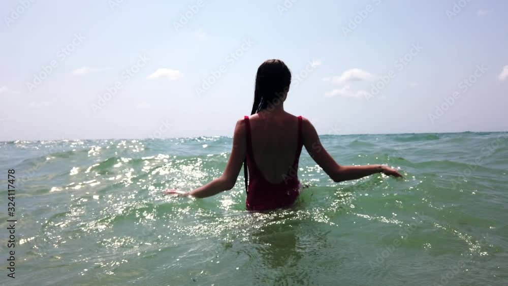 Young beautiful sexy girl with wet hair in red swimming suit going in the sea. Swimming. Sea waves. Water surface. Blue sky. Summer time vacation. Super slow motion. Young beautiful sexy girl with wet hair in red swimming suit going in the sea. Swimming. Sea waves. Water surface. Blue sky. Summer time vacation. Super slow motion.