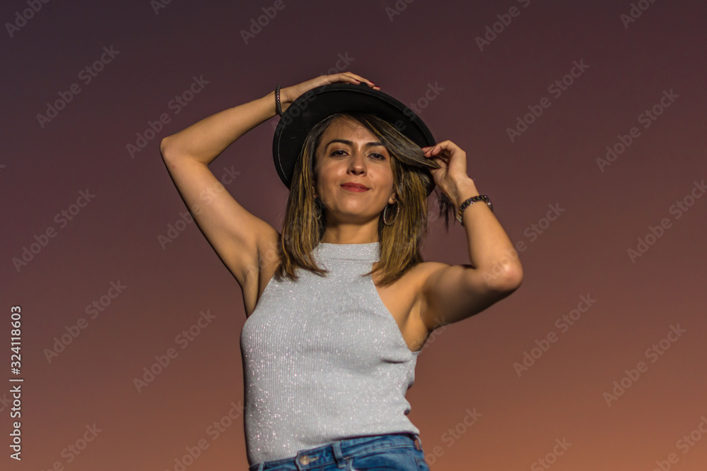 Portrait of a young attractive latin woman with black hat at sunset summer light in background Portrait of a young attractive latin woman with black hat at sunset summer light in background