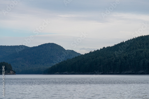 far away view of dense green forest covered islands on the ocean with mountain range over the horizon under cloudy sky 
