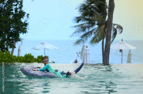 Boy wear goggles on floater in swimming pool with water splash on blur beach background