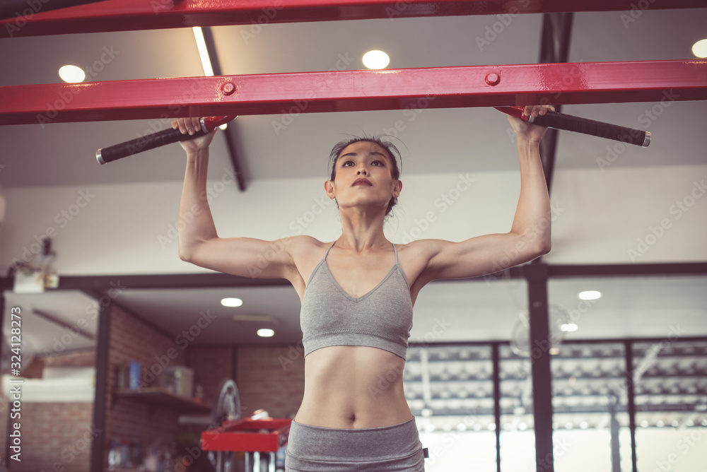 female adults doing pull ups on bar in cross fit training gym. photo of  muscular woman