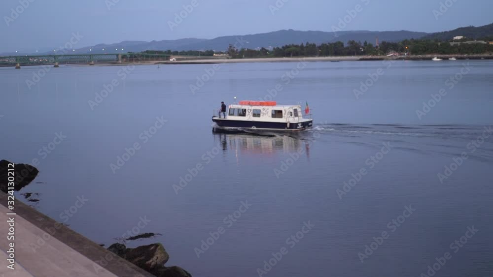Small boat crosses a river at dusk in Viana do Castelo, Portugal Small boat crosses a river at dusk in Viana do Castelo, Portugal