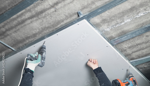 Obraz na płótnie Worker with a drill screwdriver twists the screw into the drywall