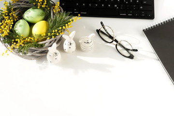 Easter background. office table desk, workspace with laptop, easter bunny,  bouquet yellow mimosa flowers, notebook on a white background.Copy space