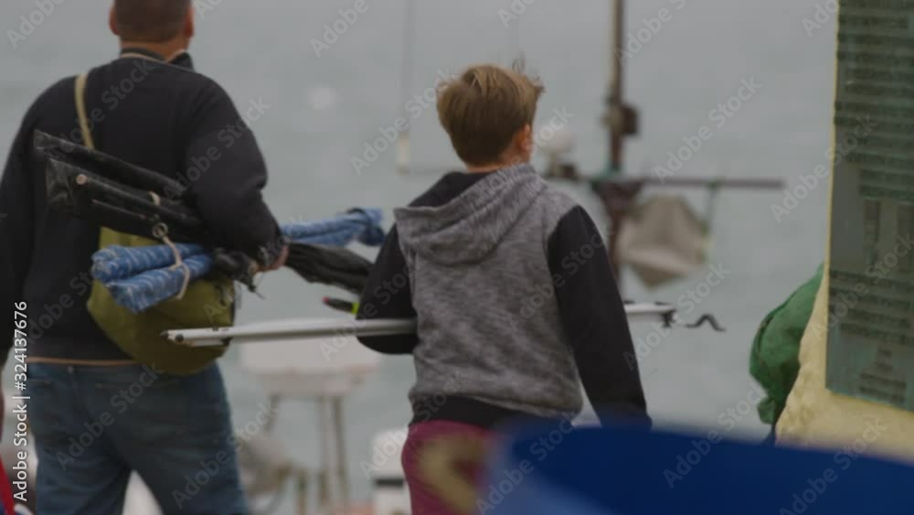 Shot from behind of a boy and his dad walking along the beach carrying fishing gear Shot from behind of a boy and his dad walking along the beach carrying fishing gear