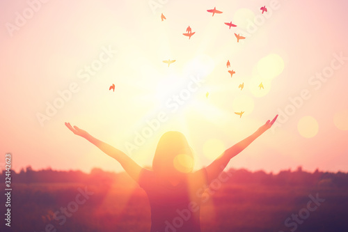 Freedom and feel good concept. Copy space of silhouette woman rising hands on sunset sky background.