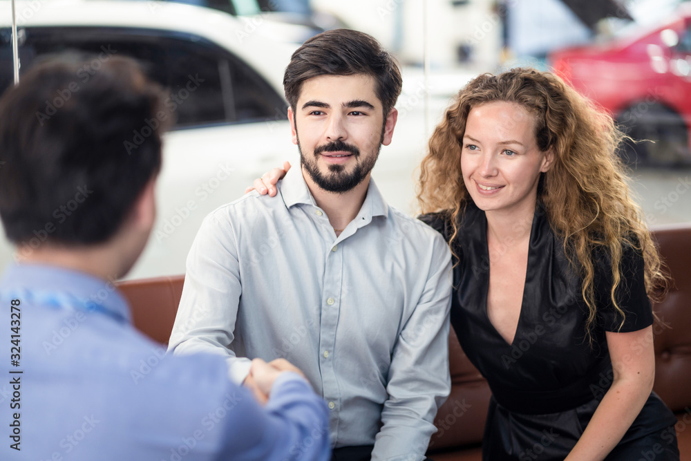 Happy Caucasion couple getting great deal and complete agreement from car rental company officer. Man customer handshake with Asian male staff sitting in office while woman satisfy service with smile. Happy Caucasion couple getting great deal and complete agreement from car rental company officer. Man customer handshake with Asian male staff sitting in office while woman satisfy service with smile.