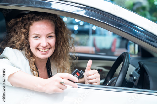 Caucasian female customer holding remote car key with smile and thumb up finger sitting in rental car. Happiness woman feeling good because get great service from car rent company. Rental car concept.
