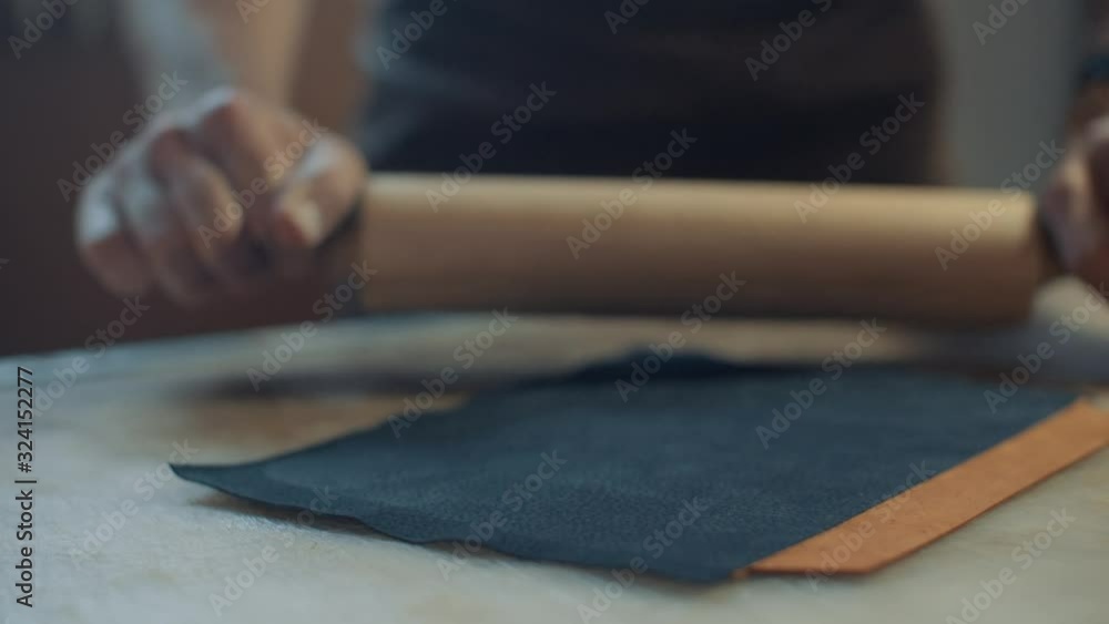 Artisan binds black and tan pieces of leather by running a rolling pin over them Artisan binds black and tan pieces of leather by running a rolling pin over them