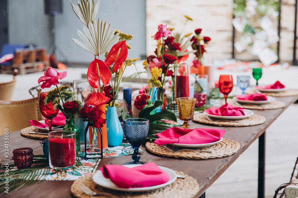 Banquet tables decorated in tropical style decor, dishes on the tables with  pink napkins, glasses, candles, colorful flowers Photos | Adobe Stock
