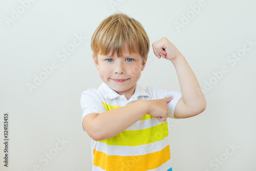 Fotografie Portrait of a strong kid showing the muscles of his arms on white background