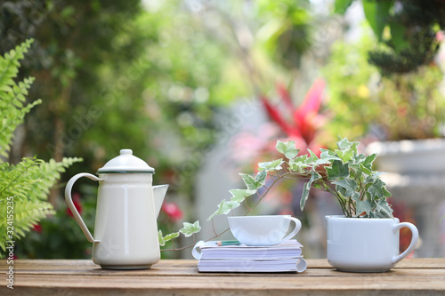 white coffee cup and Ivy plant with vintage teapot and notebook on wooden table at outdoor