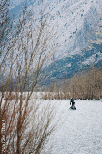 A man with warm clothes makes paddle surf exploring in a mountain lake with luggage on top of his board