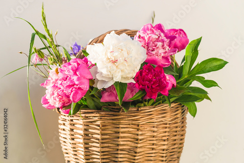 Beautiful bunch of pink, purple and white peonies in vintage wicker basket