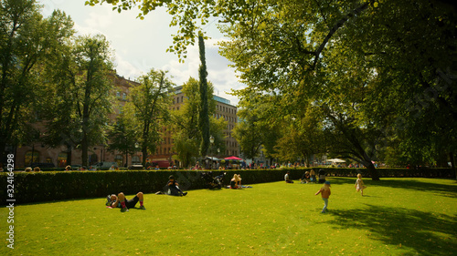Beautiful summer green park in Helsinki with adults and children resting on the grass