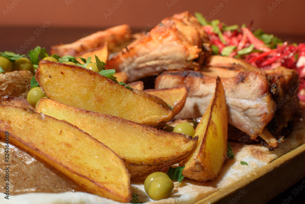 Pork ribs, rustic potato and beetroot salad on pita bread on a wooden tray. Close-up. Tasty food.