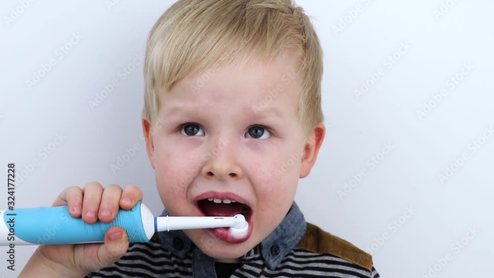 Four year old child brushes his teeth with an electric brush. The boy on a white background laughs and holds a toothbrush. The concept of baby teeth and oral hygiene Four year old child brushes his teeth with an electric brush. The boy on a white background laughs and holds a toothbrush. The concept of baby teeth and oral hygiene