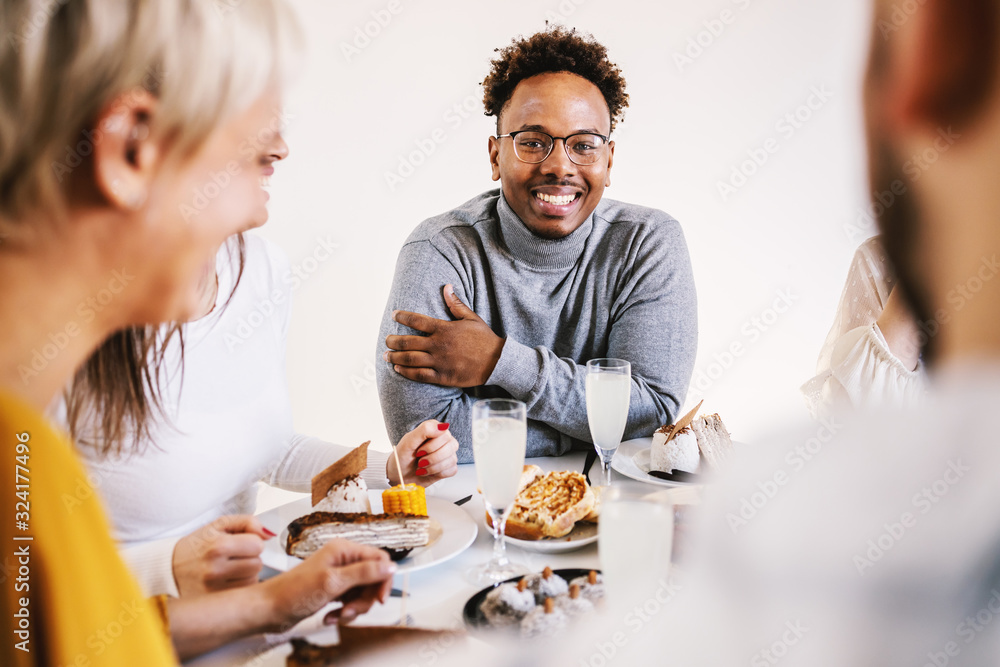 Smiling attractive african american man sitting at dinning table with friends for lunch, smiling and looking at camera.