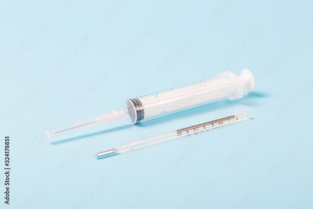 Syringe and miniature human and oral medicine and thermometer macro closeup on blue background Syringe and miniature human and oral medicine and thermometer macro closeup on blue background