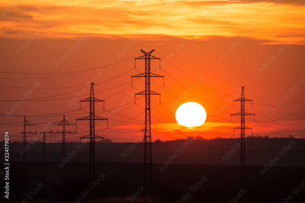 View at a Silhouette of Electric Lines and Column Pillars during Sunset with Clouds on the Sky. Beautiful sunset Nature. Rural landscape with electric pillars .