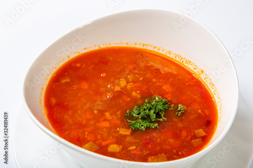 Beef goulash soup with tongue. A white oval plate with red soup stands on a white background