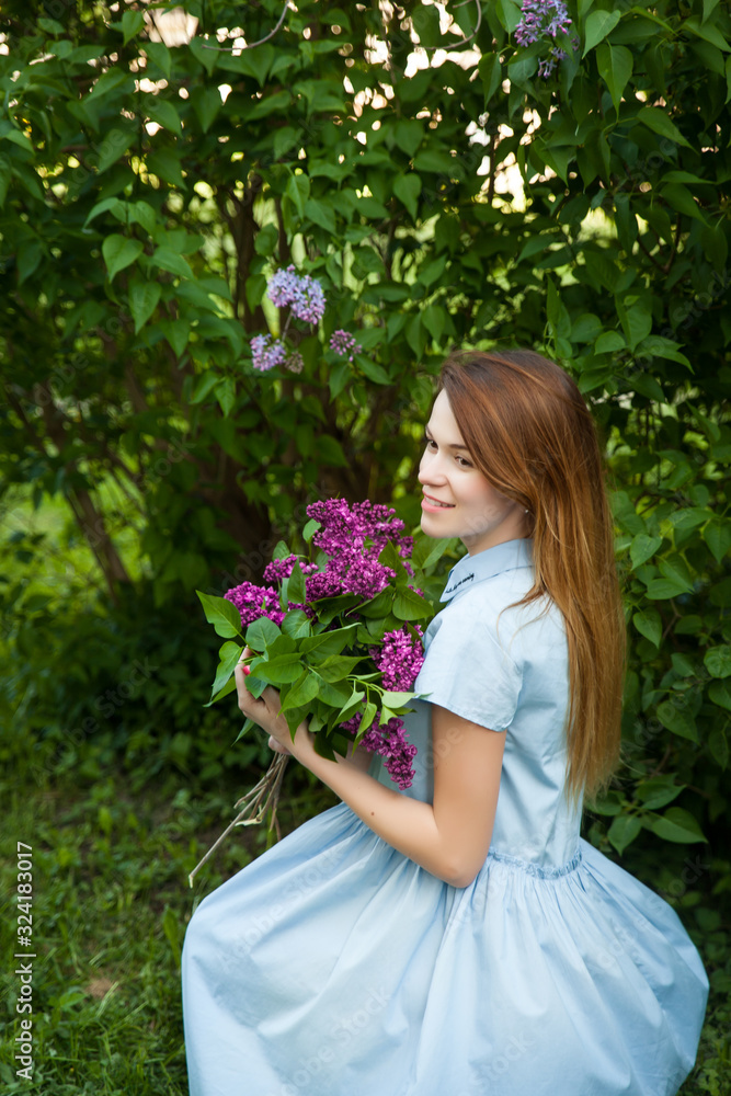 Beautiful woman in a blue summer dress with lilac flowers in a blooming garden Beautiful woman in a blue summer dress with lilac flowers in a blooming garden