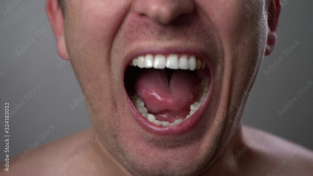 Man with angry facial expression is screaming out loud. Portrait of a shouting man with mouth wide open. Furious yelling man. Anger emotions. Anger. Violence. Mouth and grin close-up. White teeth. Man with angry facial expression is screaming out loud. Portrait of a shouting man with mouth wide open. Furious yelling man. Anger emotions. Anger. Violence. Mouth and grin close-up. White teeth.