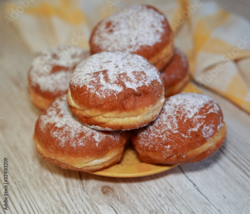 Donuts sprinkled with powdered sugar, some in soft focus, close up on wooden table, kitchen cloth