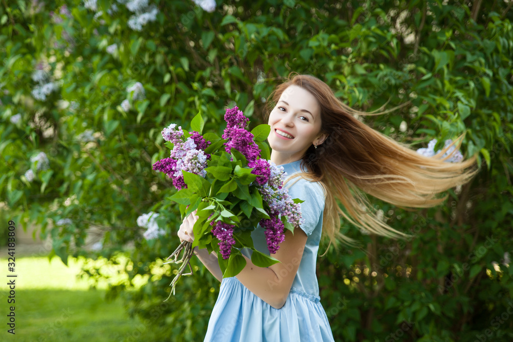 Beautiful woman in a blue summer dress with lilac flowers in a blooming garden. Spring Blossom. Beautiful woman in a blue summer dress with lilac flowers in a blooming garden. Spring Blossom.