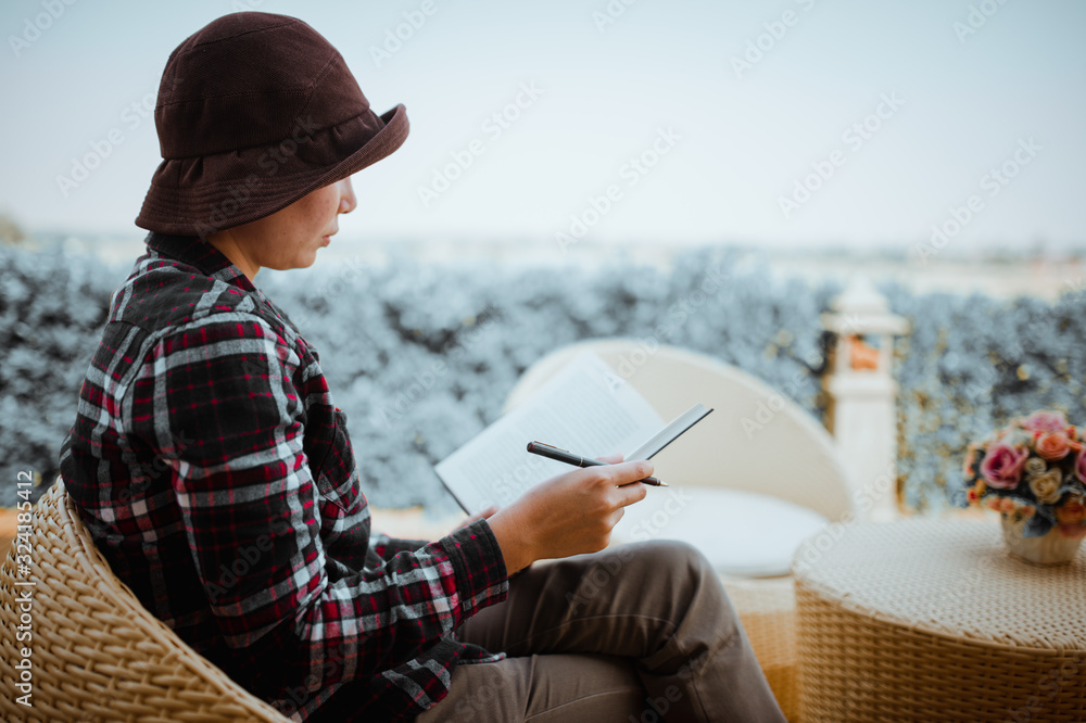 Young woman sitting in backyard, reading book and relaxing. Blurred background.Horizontal, film effect.
