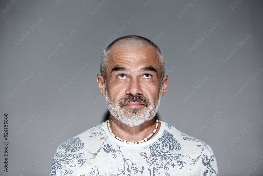 Friendly mature man with short hair and white grey beard looking upwards  over gray wall Stock Photo | Adobe Stock