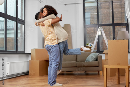 moving, repair and real estate concept - happy african american couple with cardboard boxes hugging at new home