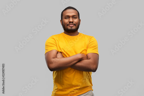 people concept - young african american man in yellow t-shirt with crossed arms over grey background
