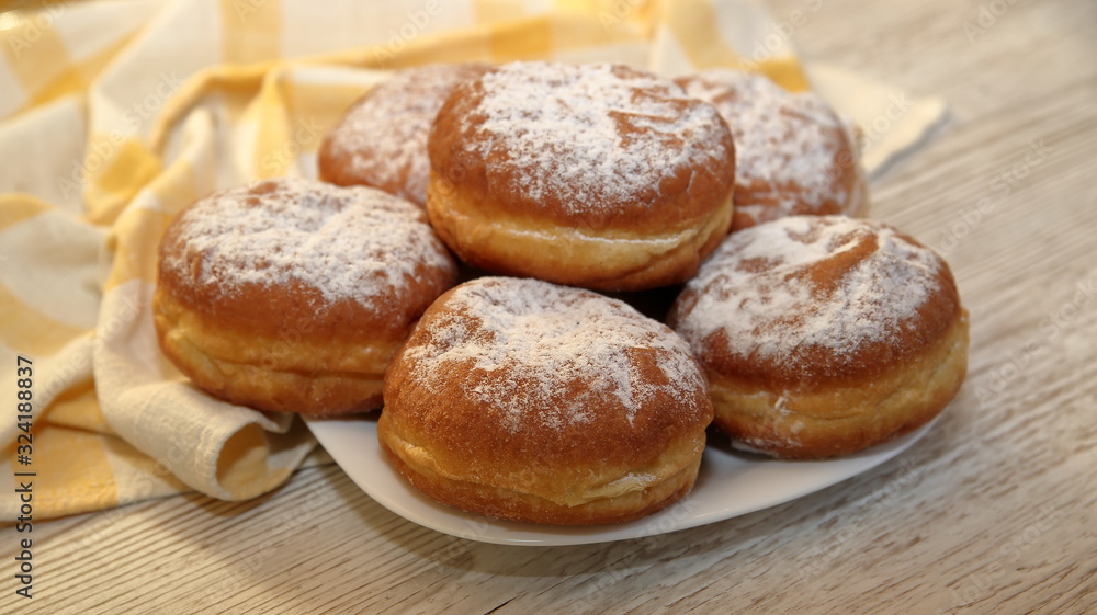Donuts sprinkled with powdered sugar, some in soft focus, close up on wooden table, kitchen cloth