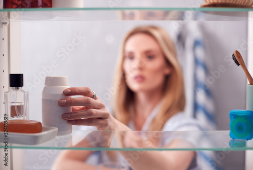 View Through Bathroom Cabinet Of Young Woman Taking Medication From Container