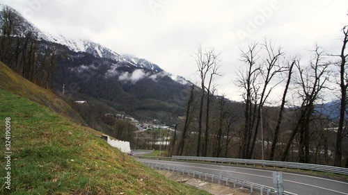 Breathtaking landscape of a mountain road and a moving car on cloudy background with snowy mountain. Stock footage. Mountain serpentine road with driving vehicle. photo